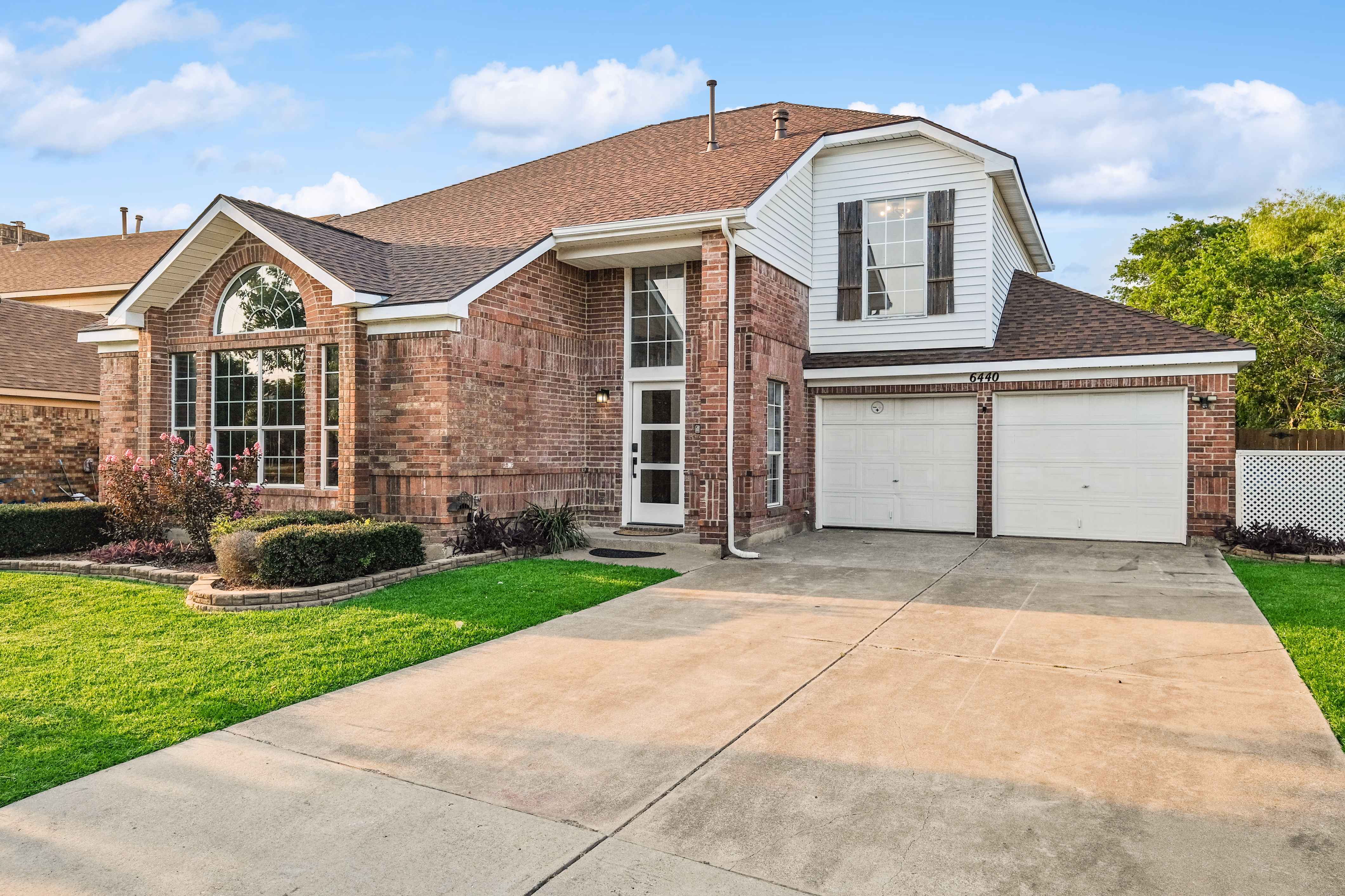 Front facade — brick two-story with two-car garage, manicured lawn.