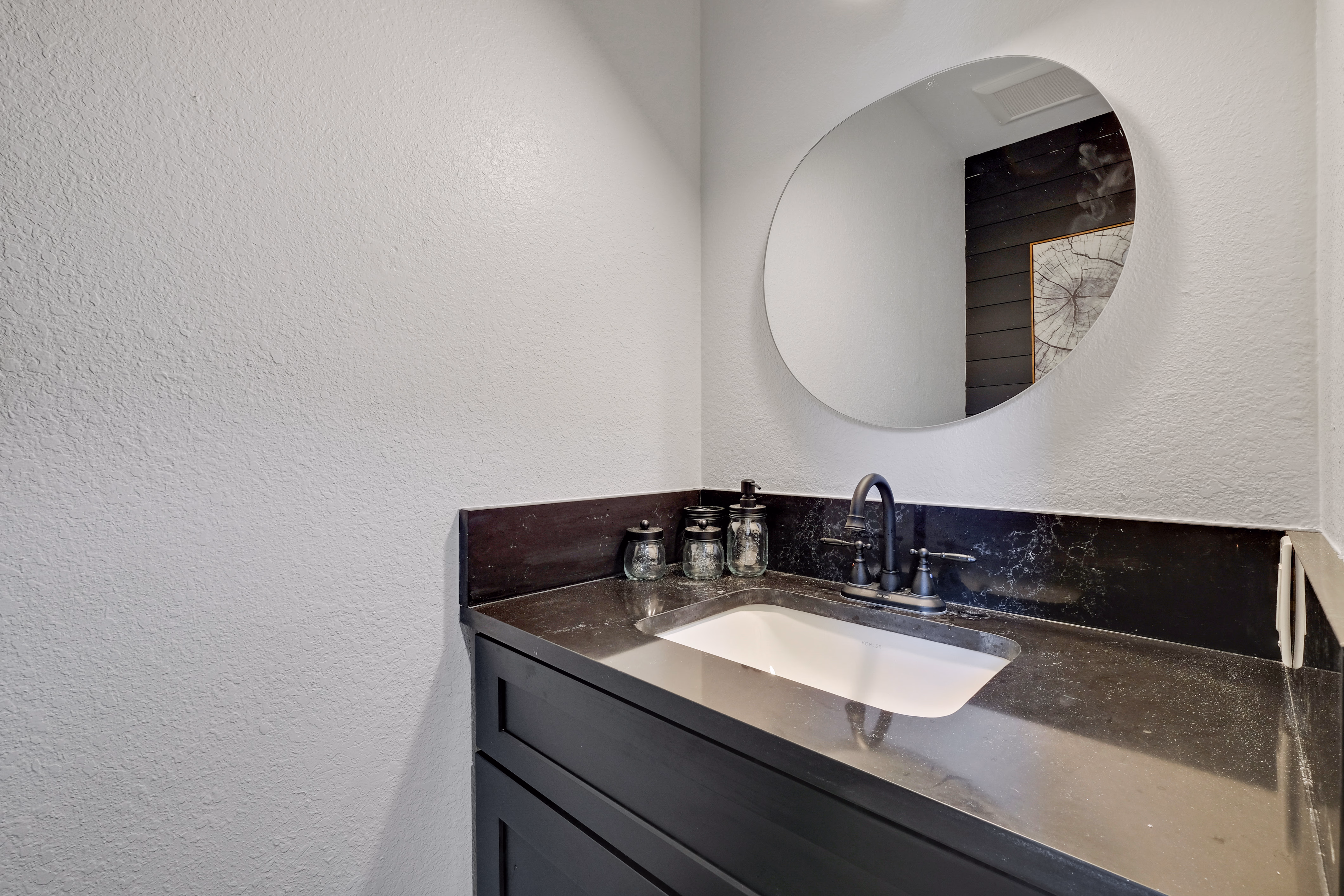 Half bath — dark vanity, round mirror, undermount sink.