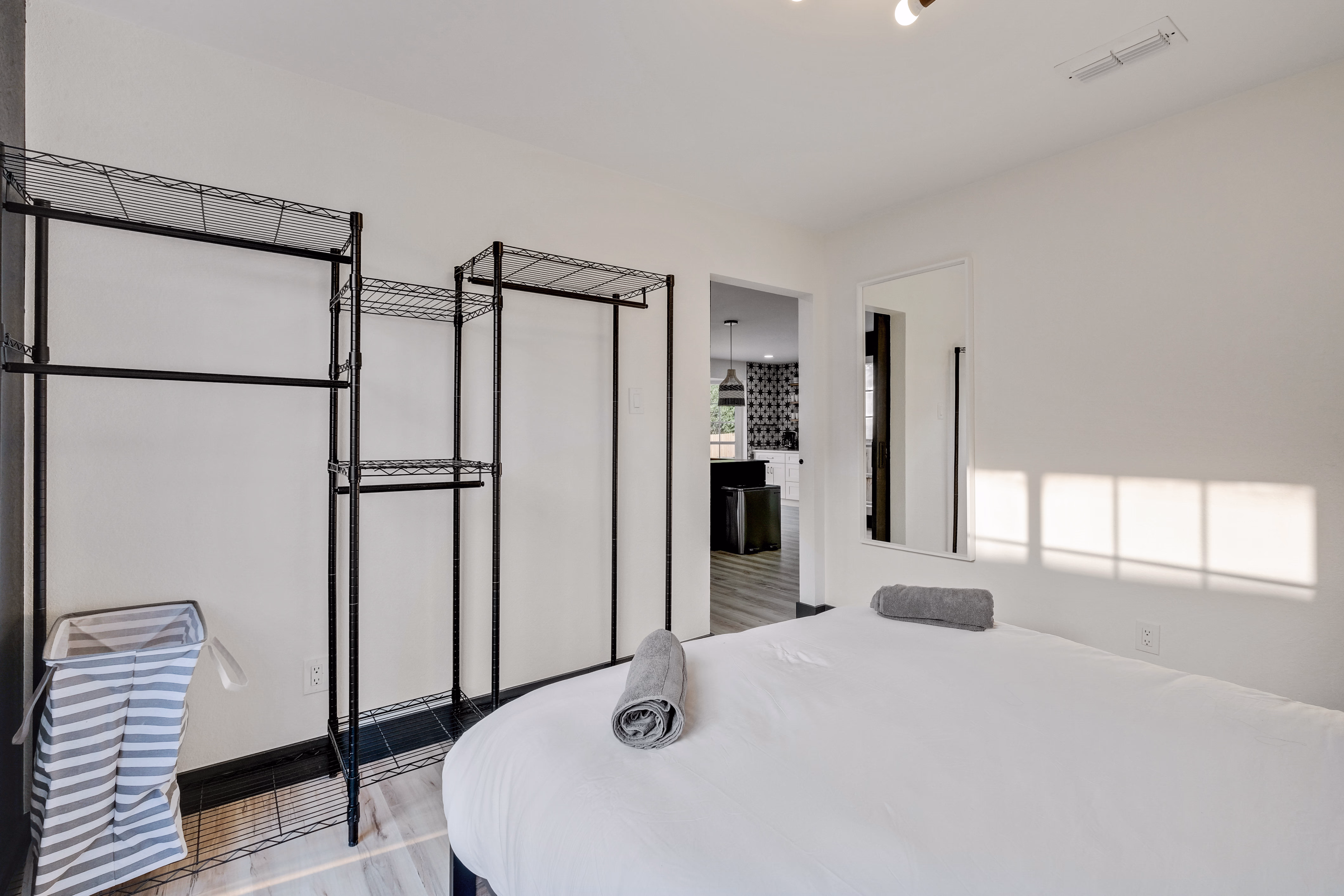 Bedroom — bed with open wire wardrobe, view into kitchen.