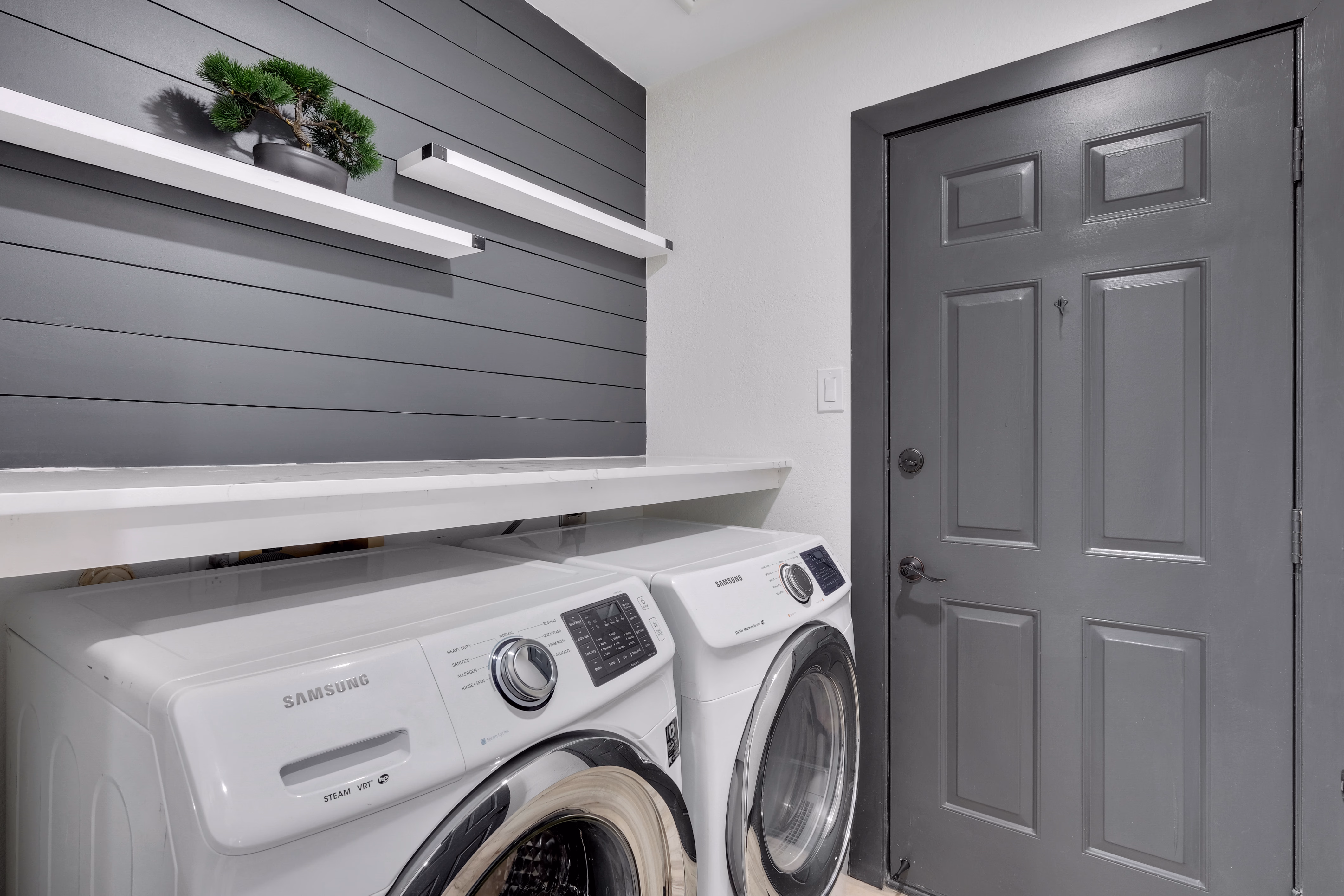 Laundry room — stacked Samsung washer and dryer with shelving.