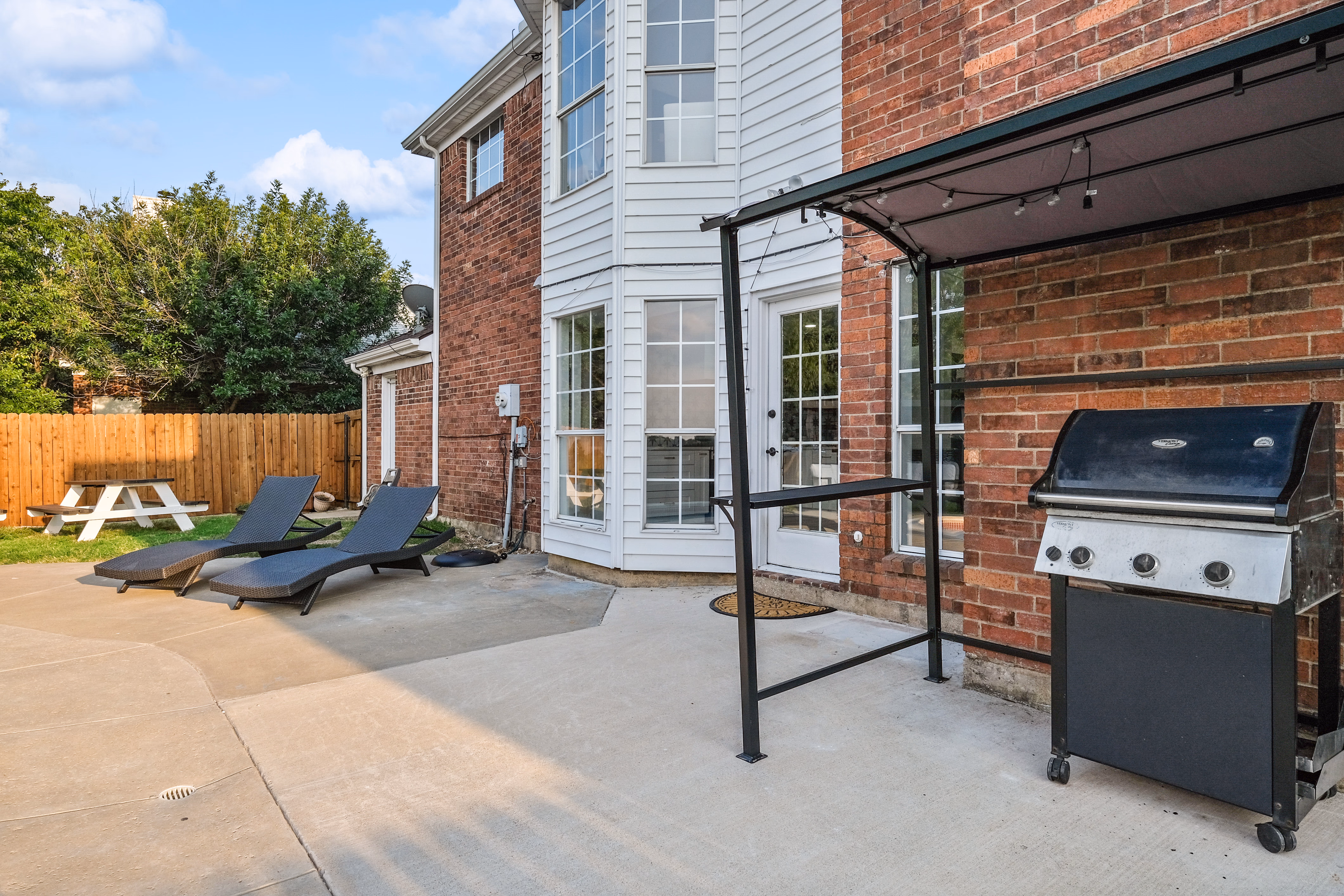 Back patio — chaise loungers, BBQ grill, pergola, brick wall.