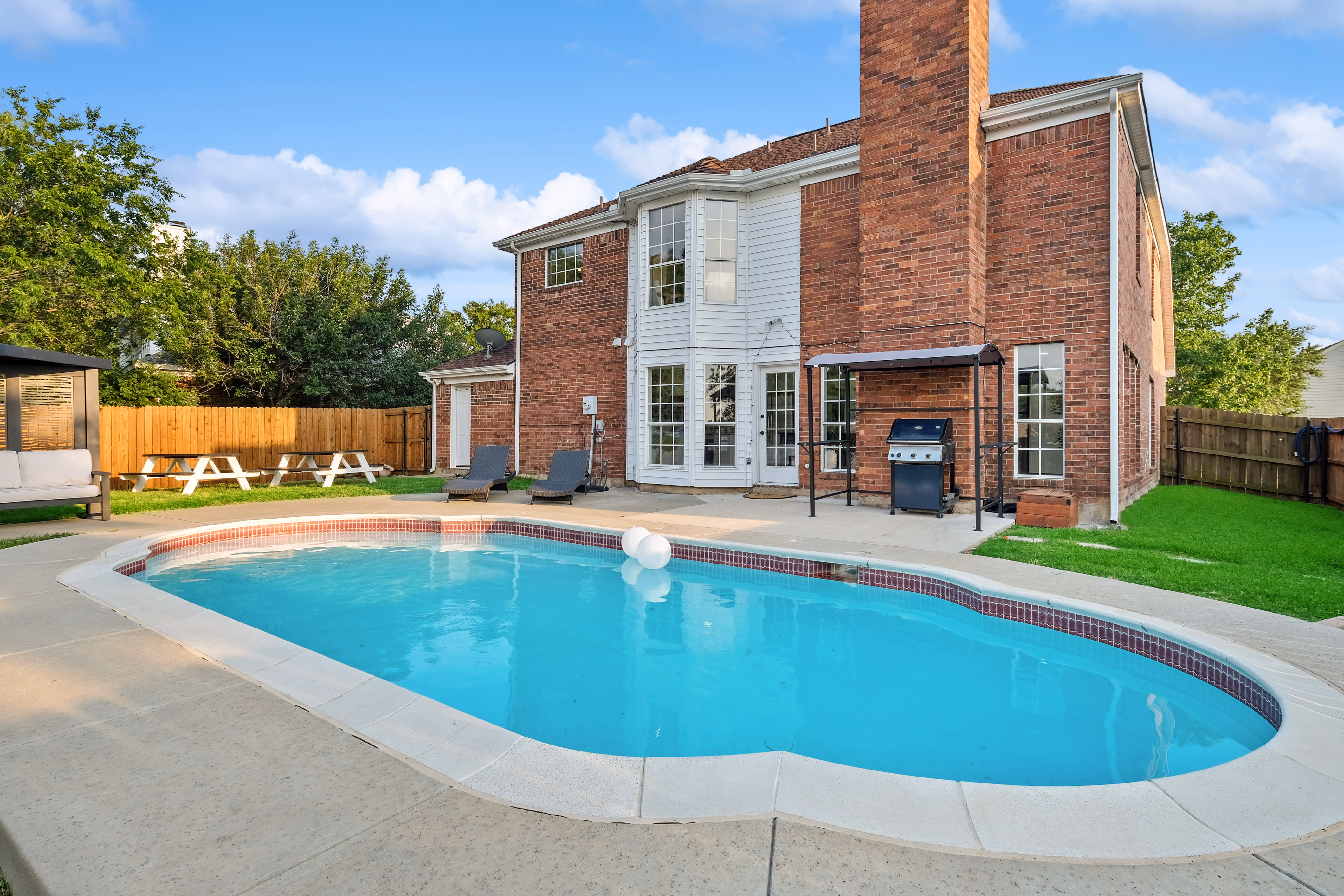 Backyard pool with house, BBQ, and chaise loungers behind.