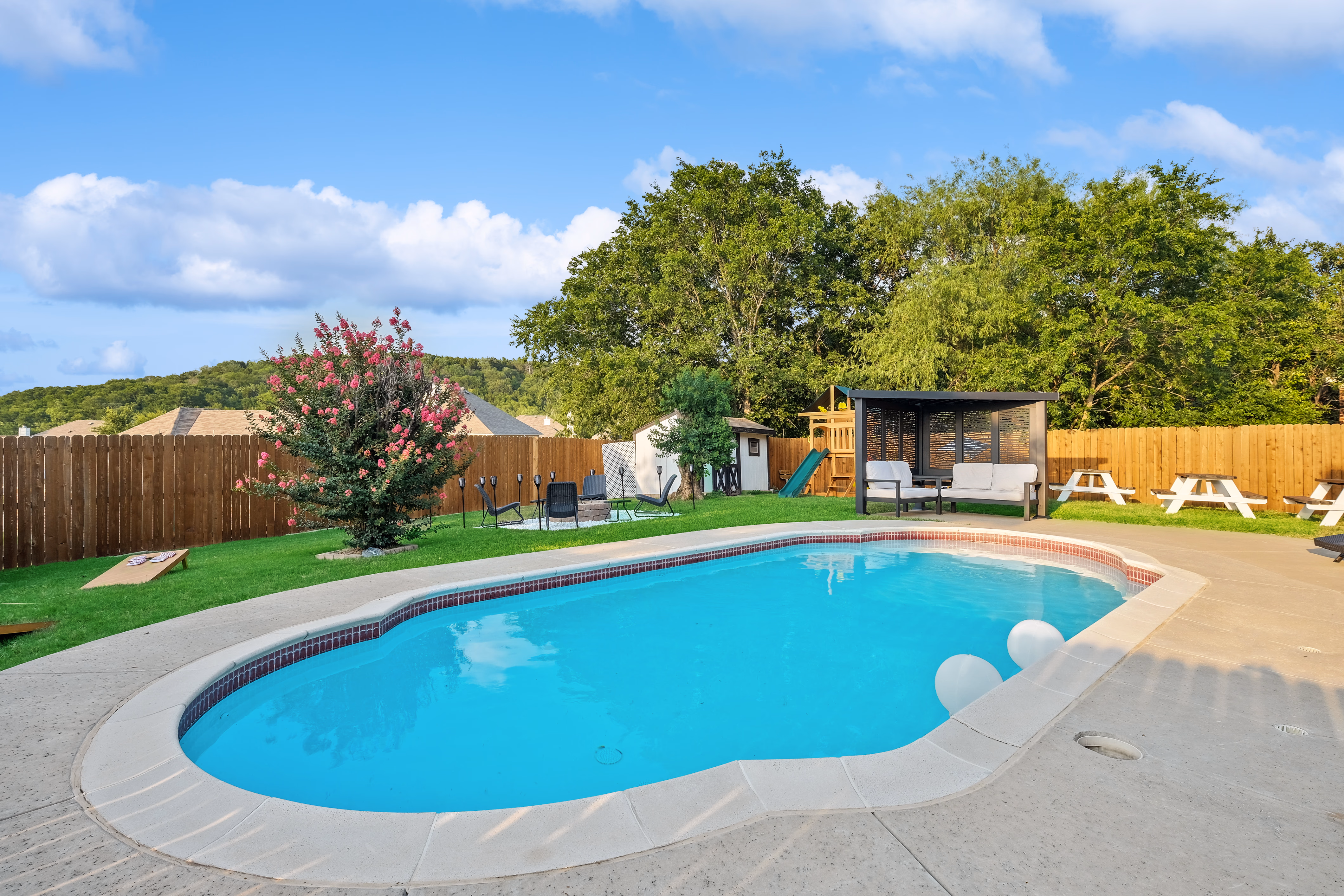 Pool with cabana, picnic tables, and playset in yard beyond.