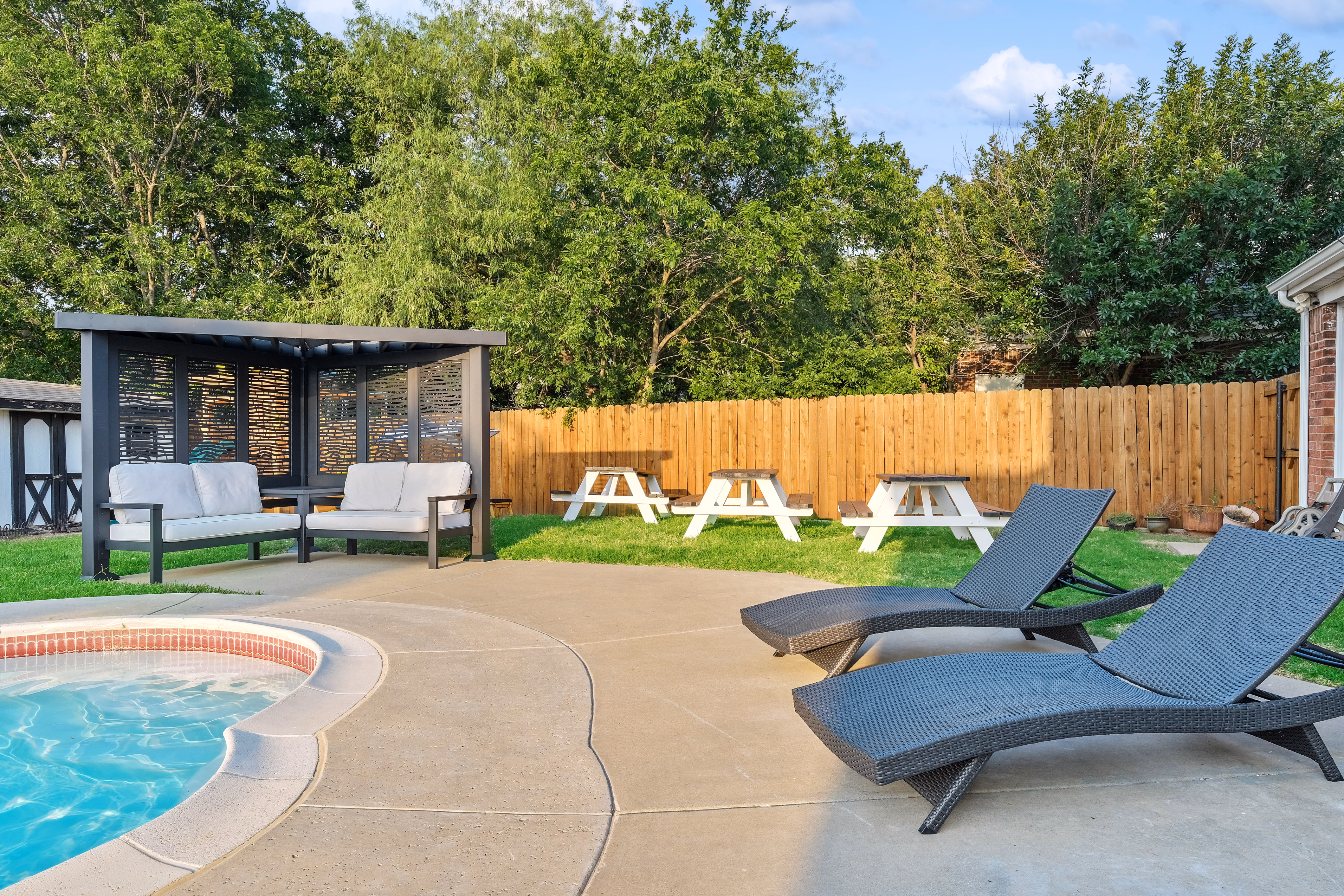 Pool, cabana with sofa, picnic tables and chaise loungers.