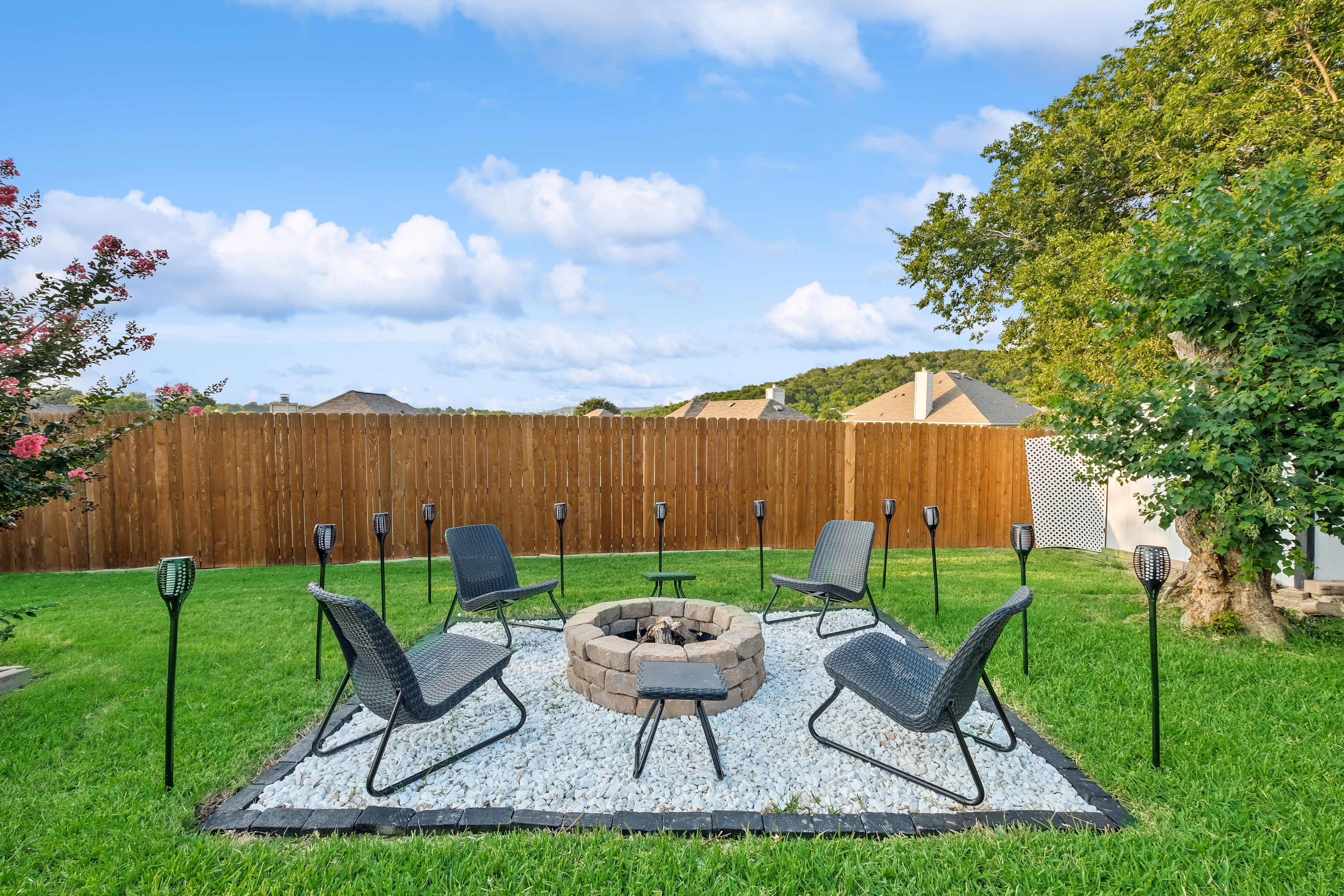 Firepit ring with four chairs and torches on gravel pad.