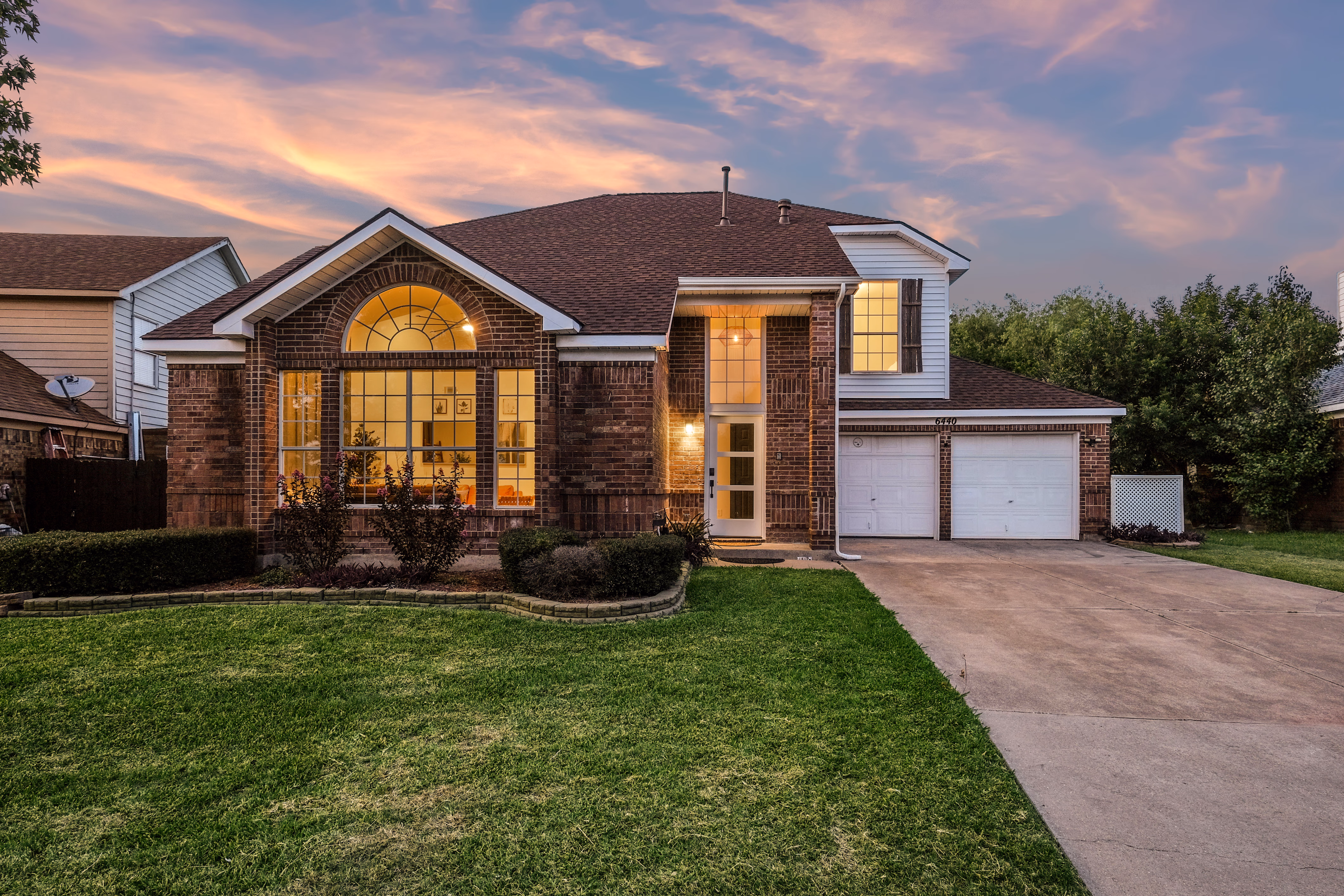 Front of house at twilight with lit windows and lawn.