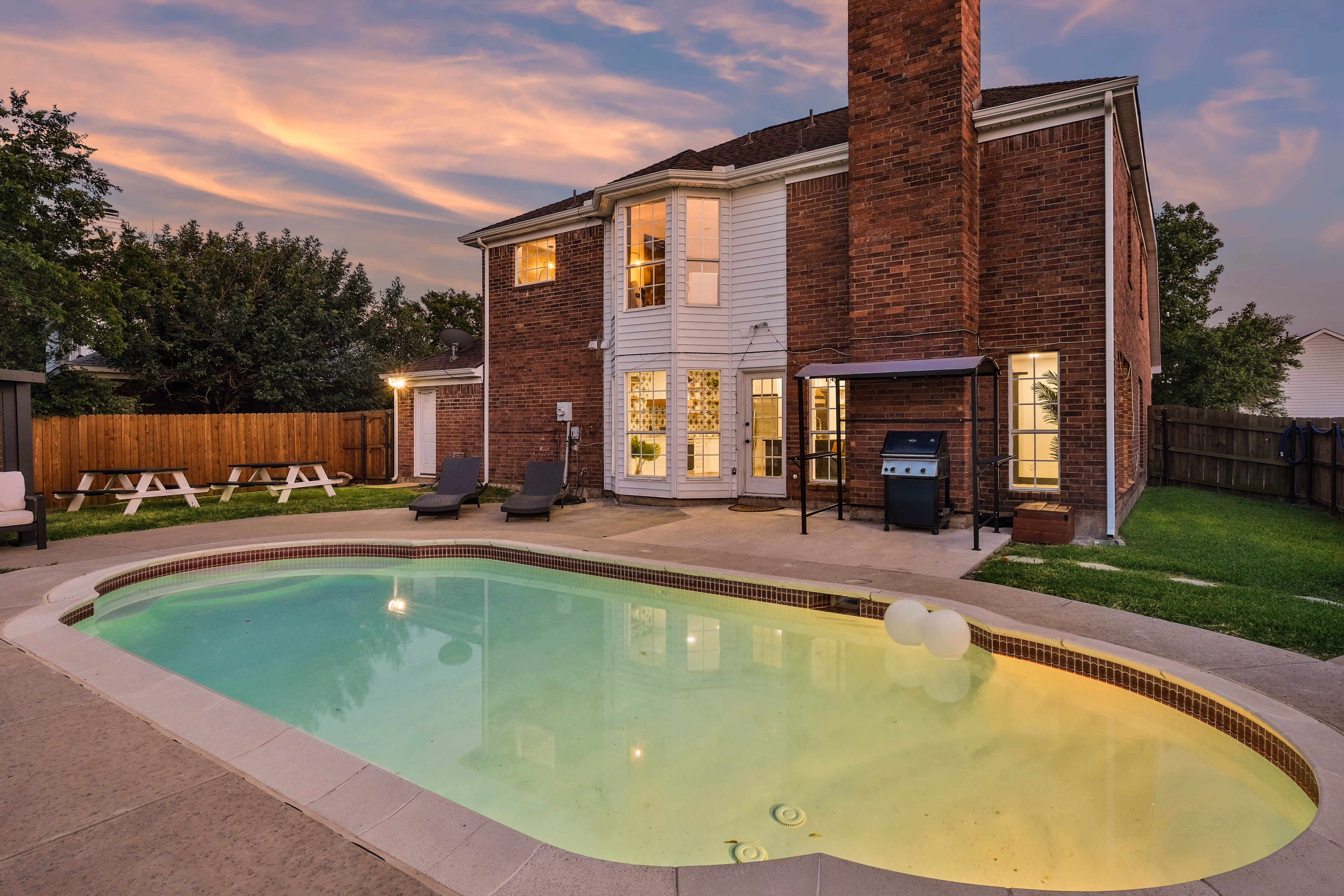 Rear of house at dusk with pool, BBQ, and warm windows.