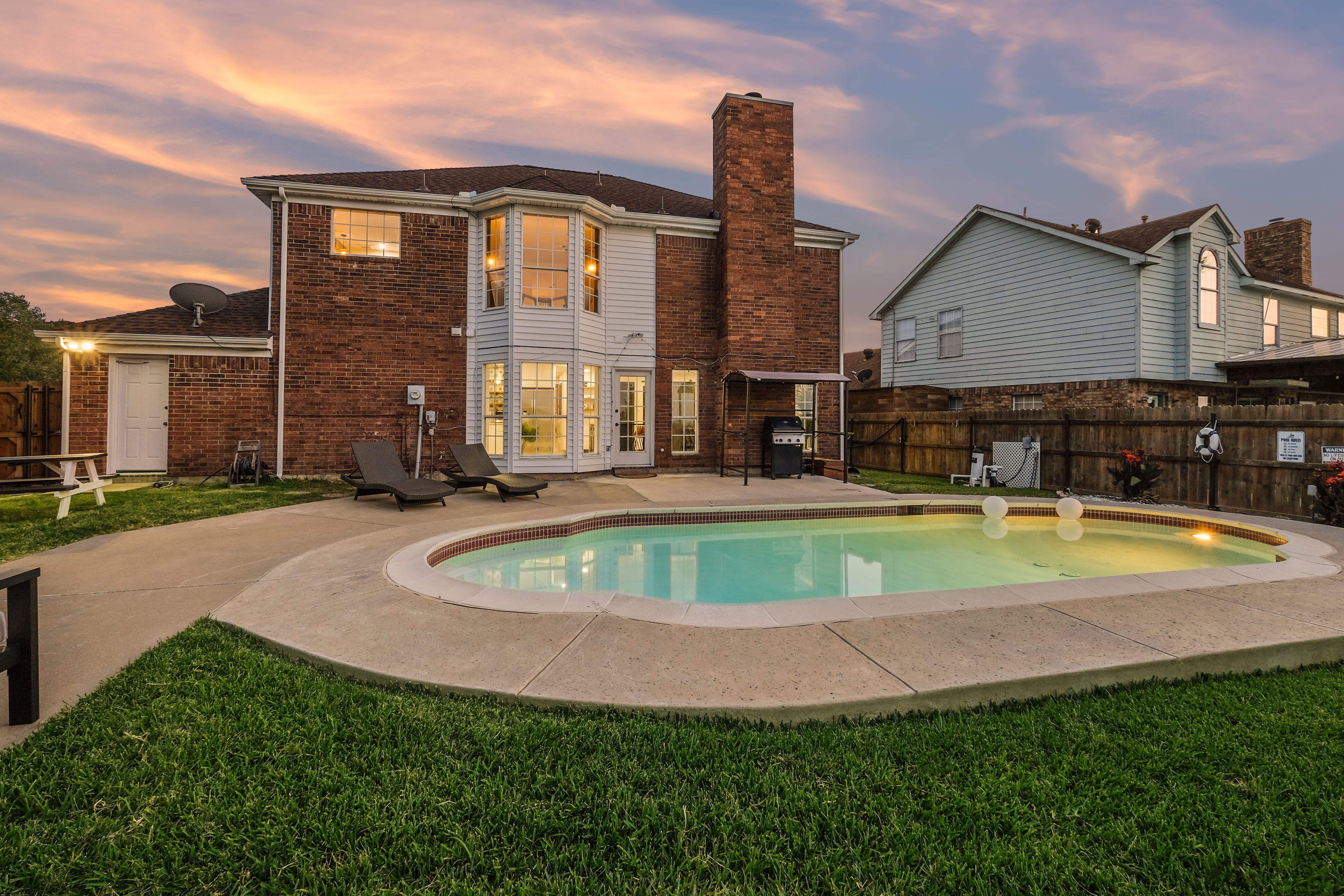 Back of house and pool at twilight, lit interior, neighbor visible.