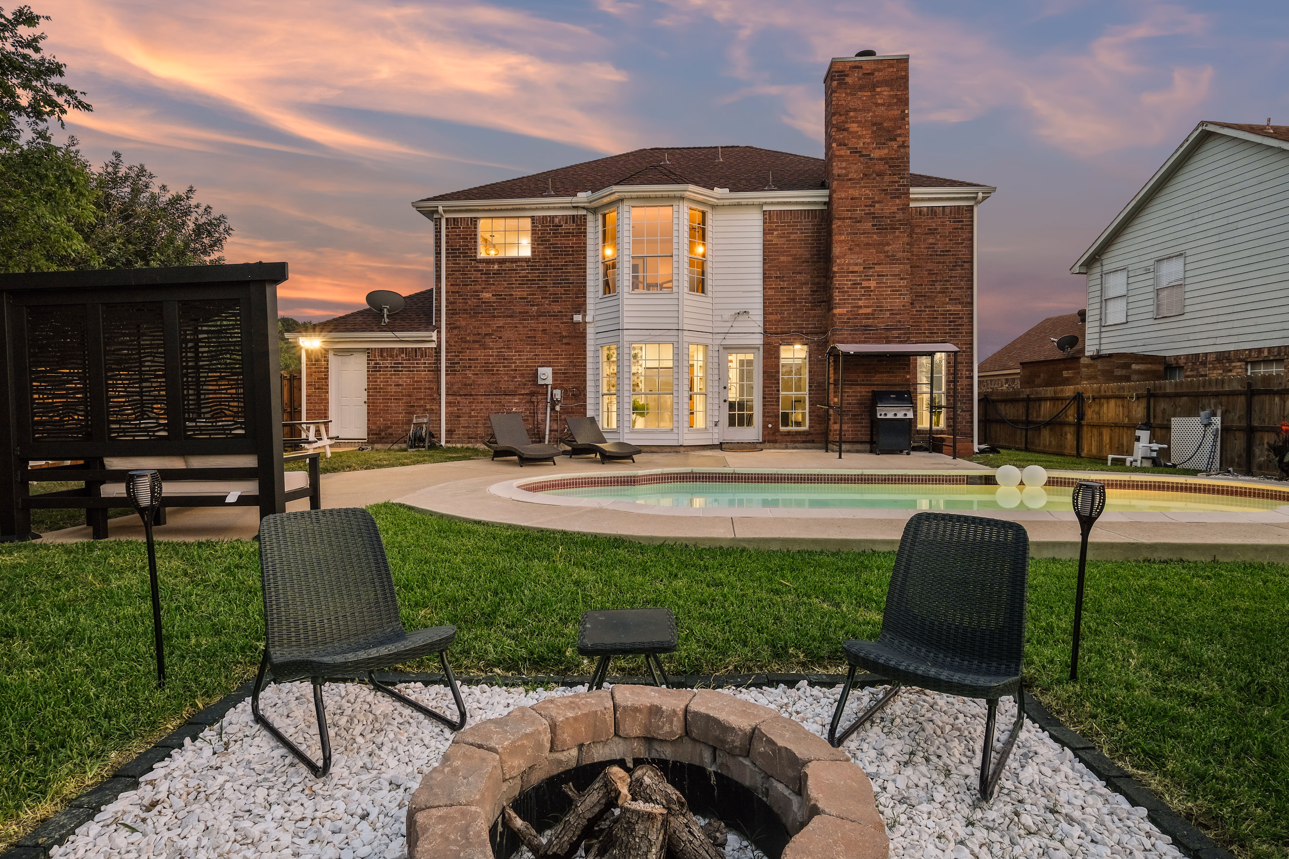 Firepit foreground with house and pool at twilight behind.